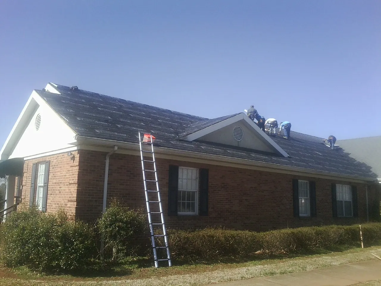 Crew tearing shingles off a brick ranch roof with a ladder set — Metal Roof Repair work by our crew in Center Point