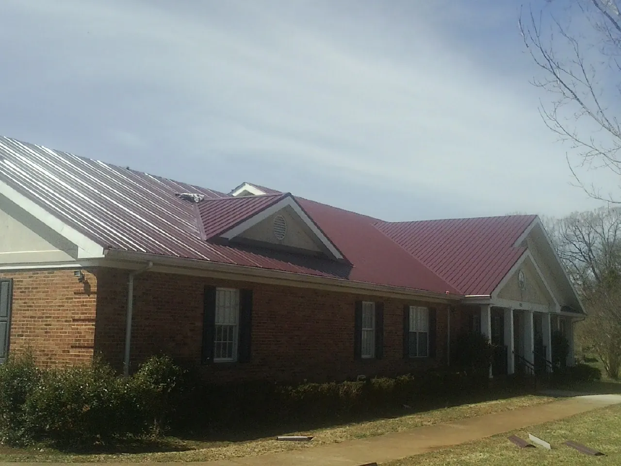 Red metal roof with gabled entries on a long brick building, from a Hail Damage Roof Repair job in Center Point