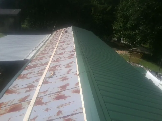 Old rusted panels beside newly installed green metal roofing — Wind Damage Roof Repair by Roofing Brothers in Center Point