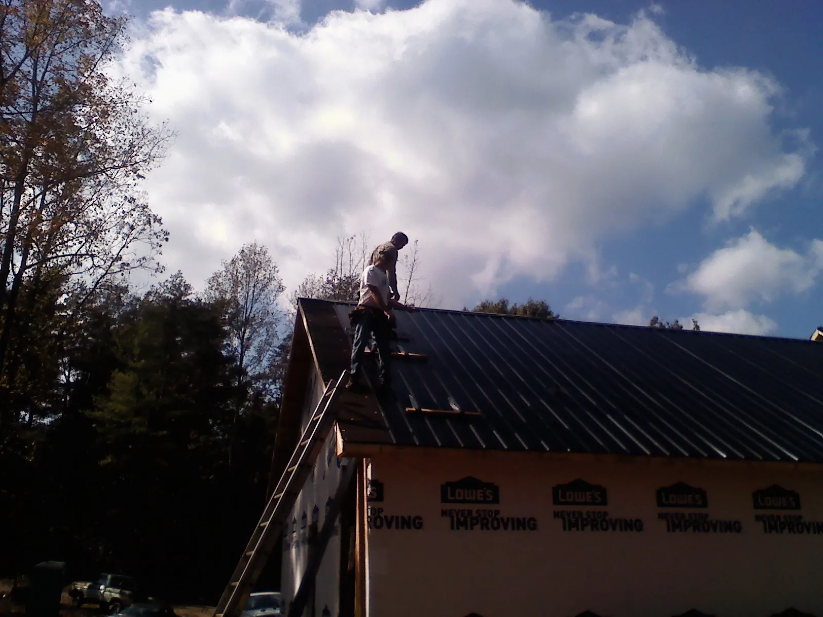 Roofer fastening dark metal panels high against a cloudy sky, from a Roof Inspection job in Center Point
