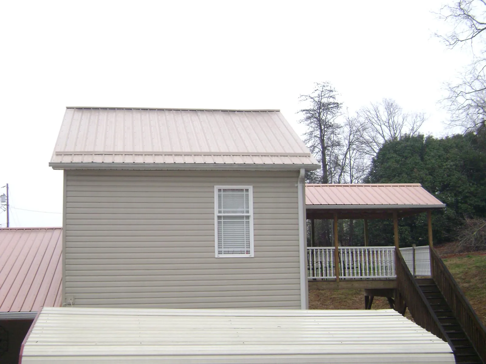 Tan metal roofs on a two story addition and attached porch, from a Roof Replacement job in Center Point